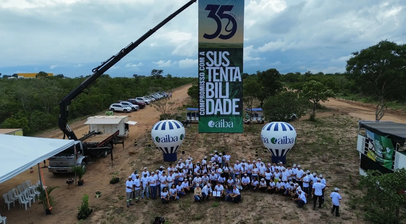 Participantes reunidos ao ar livre diante de uma sinalização da AIBA sobre compromisso com a sustentabilidade